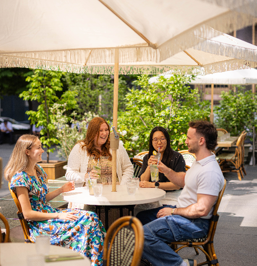 Three people enjoy a meal at a restaurant with a city view, drinks and a bottle of soda on the table.