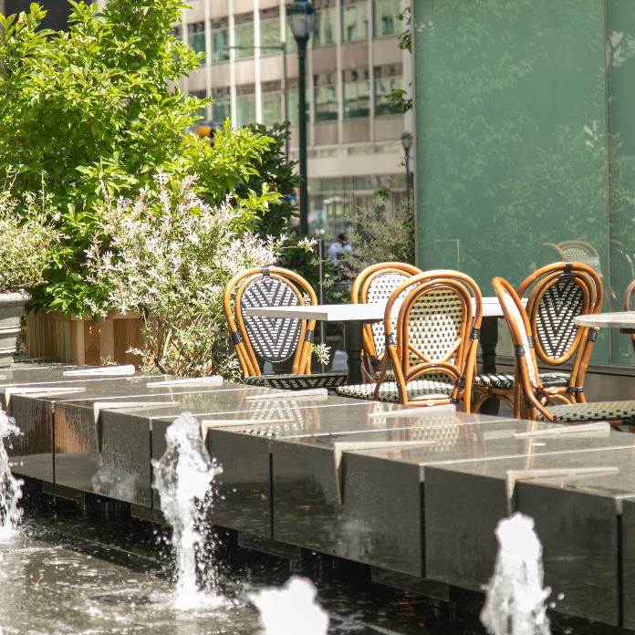 Outdoor patio seating with bistro chairs beside decorative fountain and greenery at urban restaurant